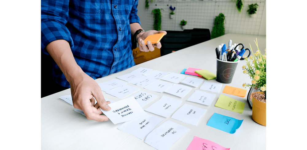 A man in a blue plaid shirt doing some work organization by setting different sticky notes next to each other